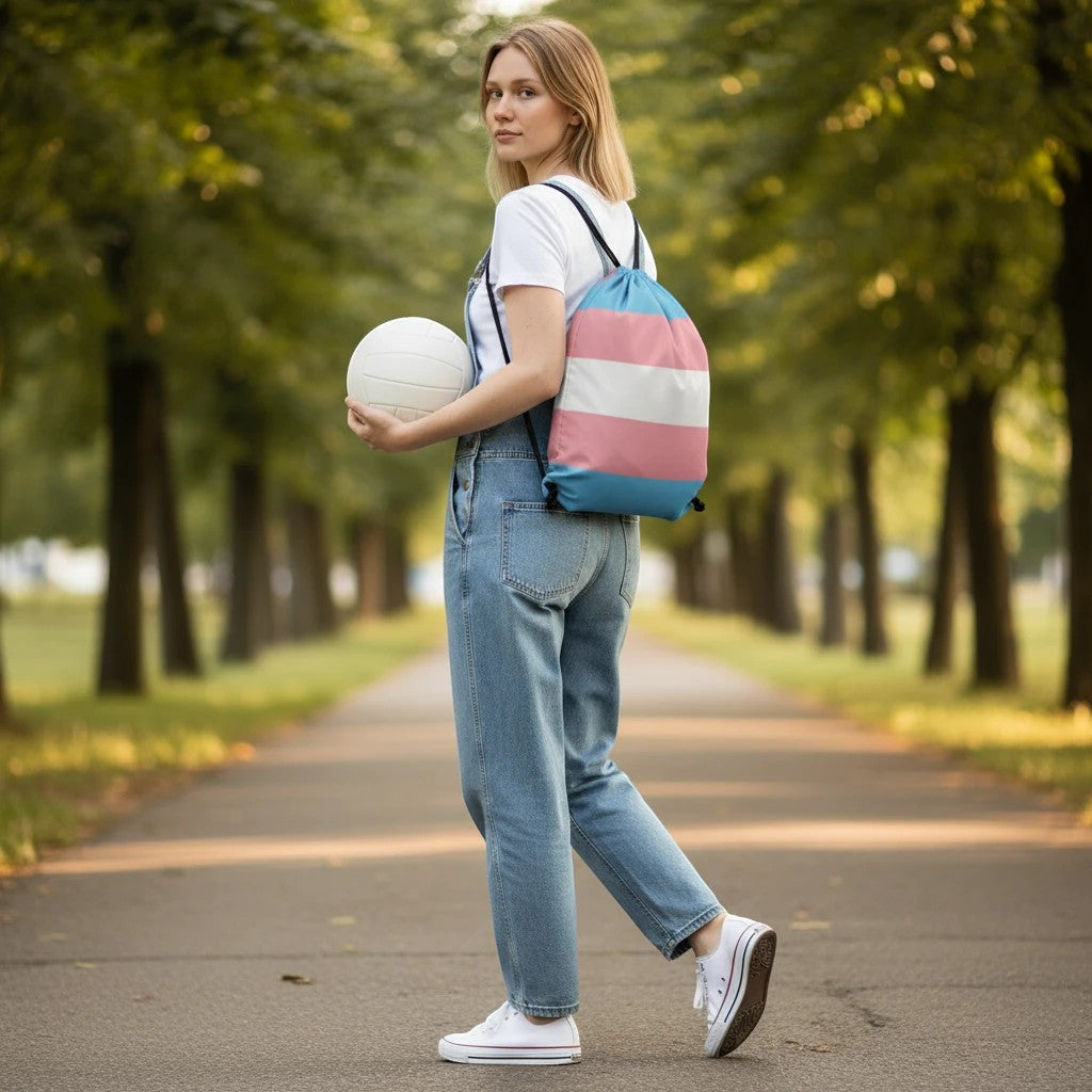 65mcmlxv transgender pride flag print drawstring bag with white and pink stripes on blue background. Model holds a white ball.